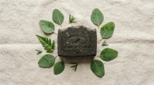 Flat lay of a charcoal soap bar for acne surrounded by fresh botanical eucalyptus leaves